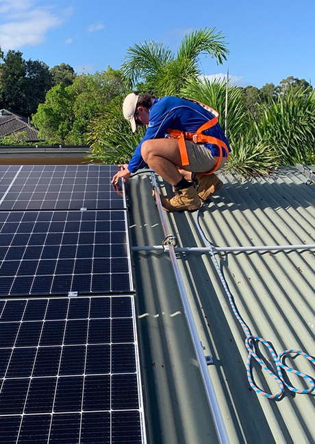 Image of a Goodhew Electrician on a roof installing solar panel while wearing a harness.